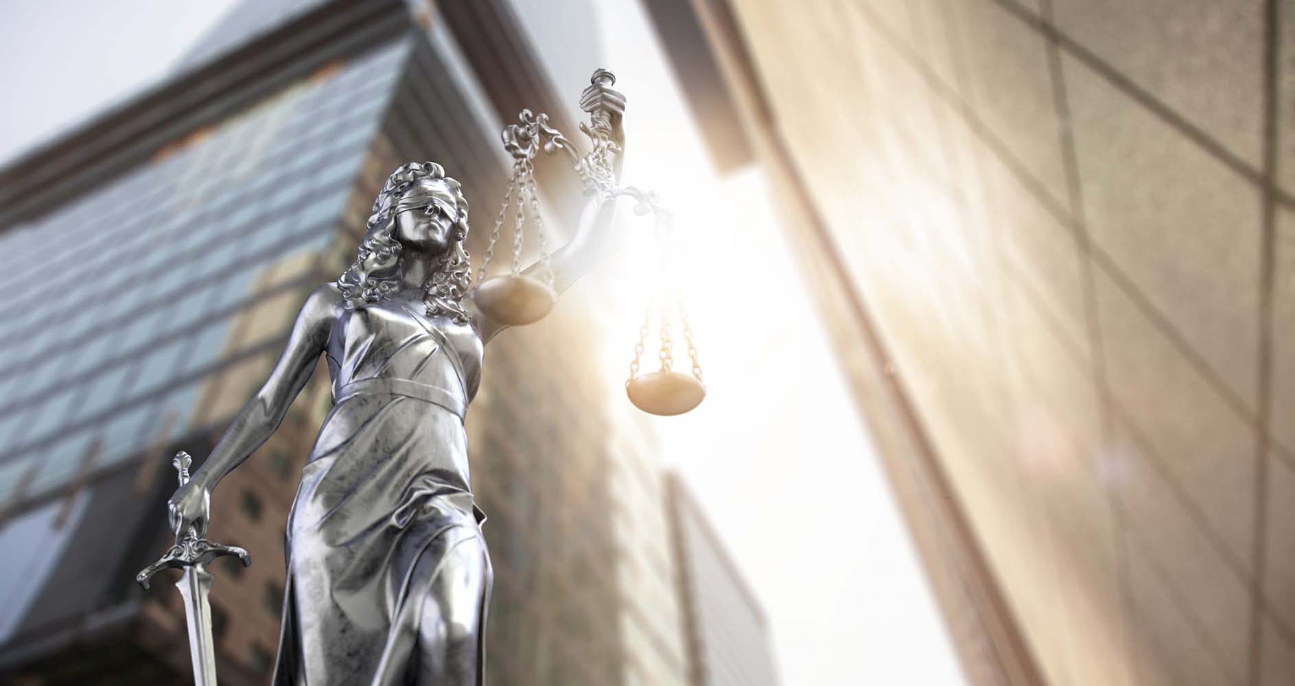 Image of the scales of justice silhouetted against buildings and the sun.